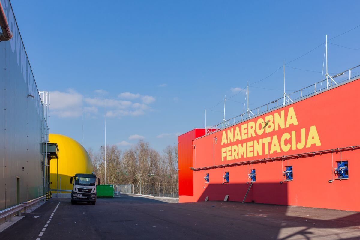 Bioreaktor, velika rdeča betonska zgradba, kjer poteka anaerobna razgradnja bioloških odpadkov. V ozadju rumen balon, plinohram, kjer se zbira izločen bioplin.