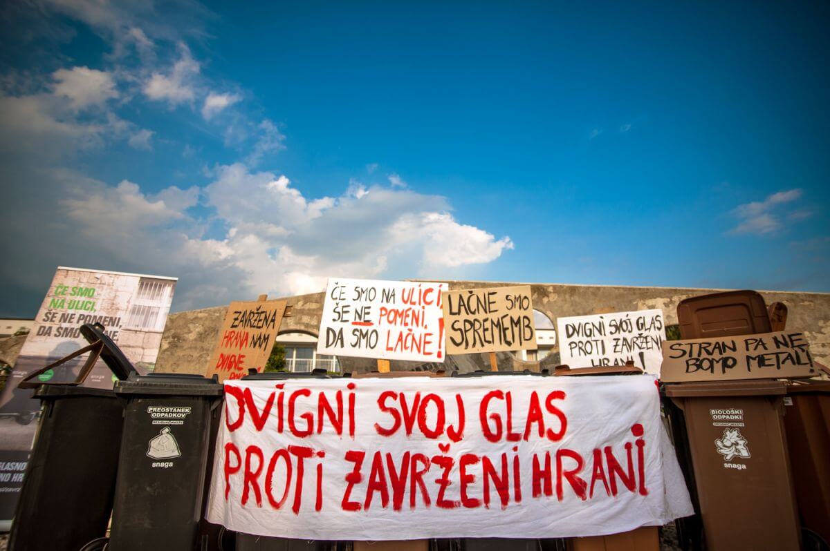 Dustbin protesr against food waste. There are banners saying "Just because we are on the streets, it doesn't mean we are hungry".