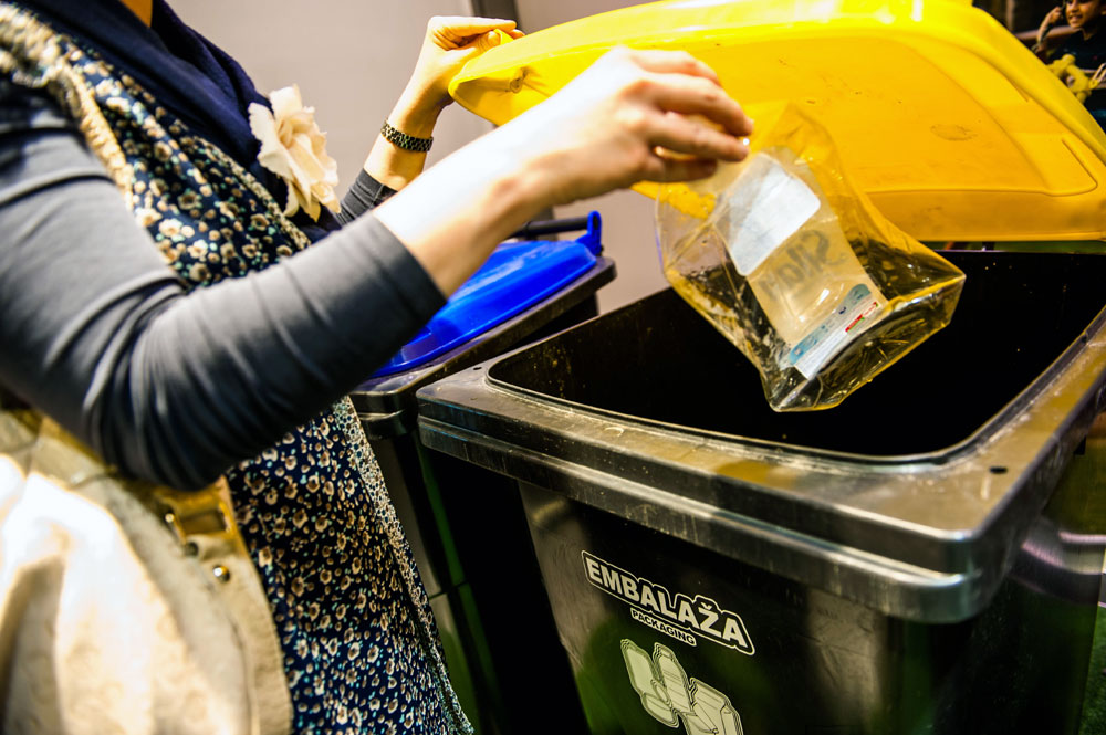 A woman putting empty shampoo plastic packaging to the yellow-lid bin.
