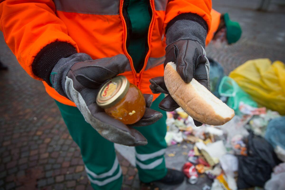 Food waste (still edible bread and a jar of honey) in hands of a waste collection woker.