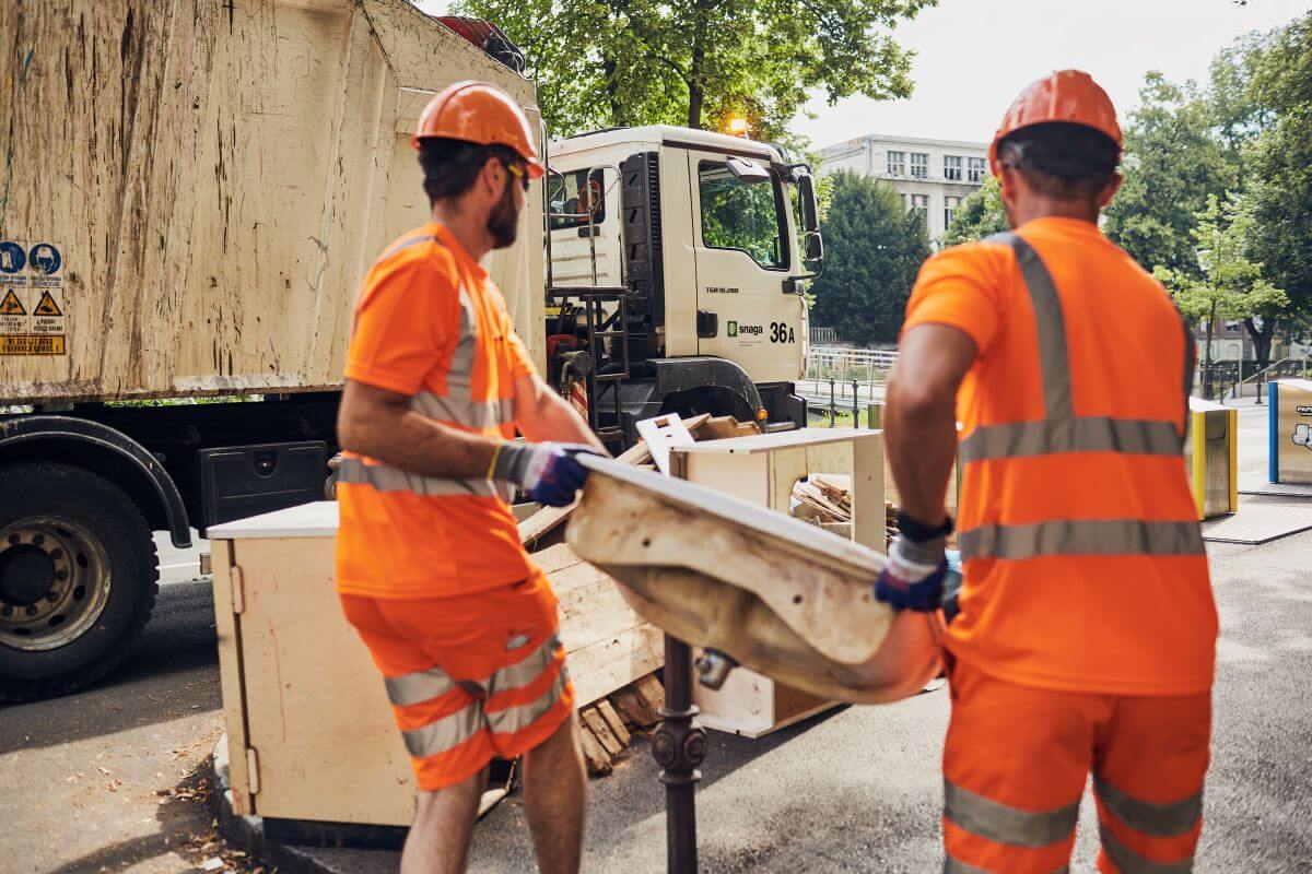 Bulky waste removal. Two workers carying an old sink closer to the waste collection truck.