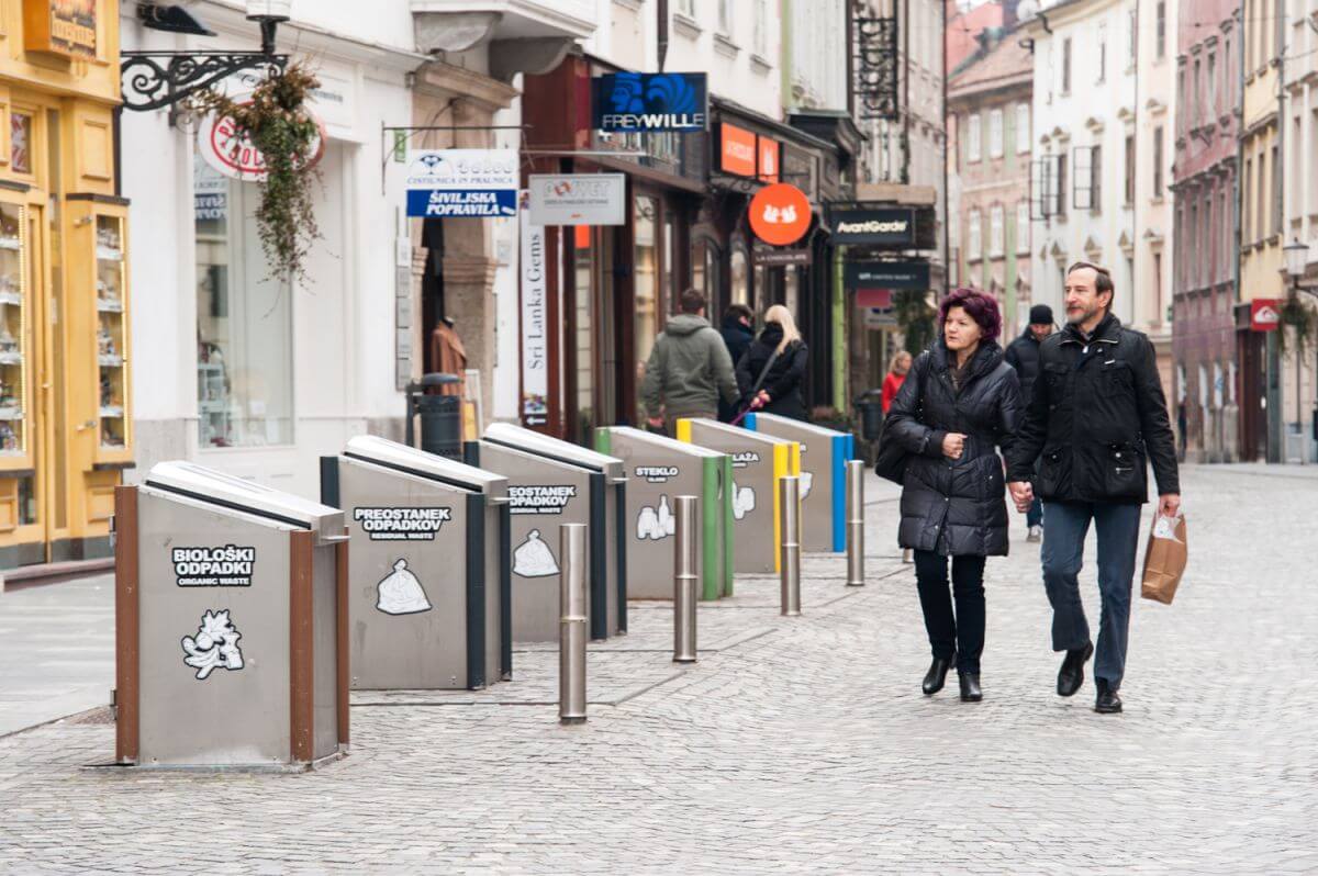 A couple passing by a underground collection unit in the Mestni trg in Ljubljana.